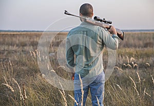 Hunter stands in the field with his back putting the gun on his shoulder