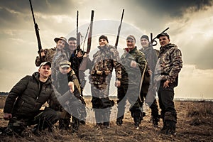 Hunters standing together against sunrise sky in rural field during hunting season. Concept for teamwork