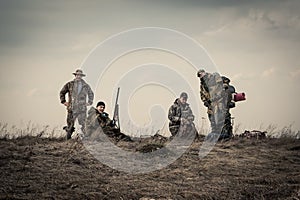 Hunters standing together against sunset sky in rural field during hunting season