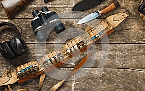 Hunting equipment on old wooden background including rifle, knife, binoculars and cartridges