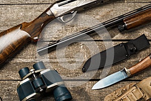 Hunting equipment on old wooden background including rifle, knife, binoculars and cartridges