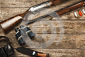 Hunting equipment on old wooden background including rifle, knife, binoculars and cartridges