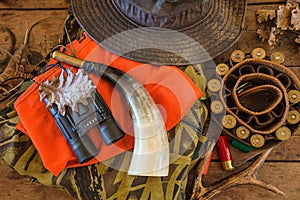 Hunting equipments on the old wooden background top view. Hunting belt, hat, camouflage, orange waistcoat, sleeves, deer antler,