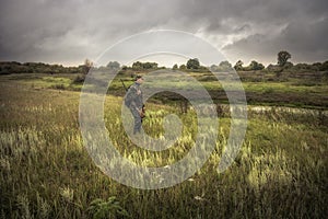 Hunting hunter men with gun standing in field nearby river during hunting season in overcast day