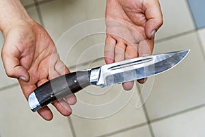 A hunting knife with a wooden handle in the hands of the seller. Sale of steel blades in a specialized store. Close-up.