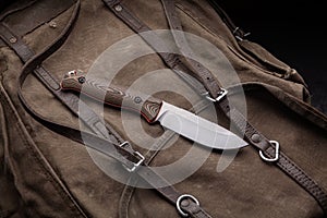 A hunting knife with a wooden handle on a khaki canvas backpack. Weapons for self-defense and survival