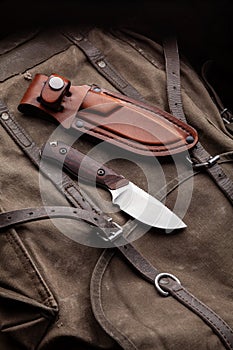 A hunting knife with a wooden handle and a leather case on a khaki canvas backpack. Weapons for self-defense and survival