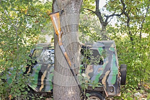 Hunting rifle hanging on a tree near an SUV