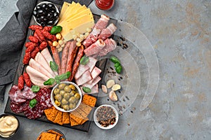 Hunting sausages, salami, bacon, ham, various types of cheese, olives and spices on a cutting board on a gray background