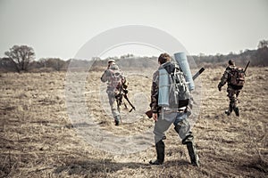 Hunting scene with group of hunters with backpacks and hunting ammunition going through rural field during hunting season in overc