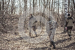 Hunting scene with group of hunters in camouflage walking in spring forest with dry leaves during hunting season