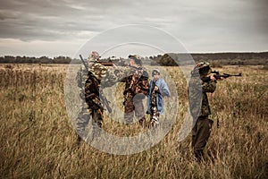 Hunting scene with hunters aiming during hunting season in rural field in overcast day with moody sky