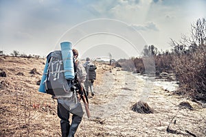 Hunting scene with hunters with backpack and hunting equipment going across rural area during hunting season