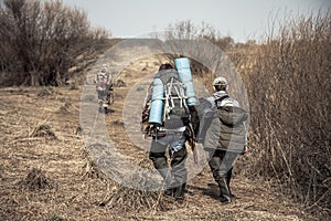 Hunting scene with hunters with backpacks and hunting ammunition going across rural area with bushes during hunting season