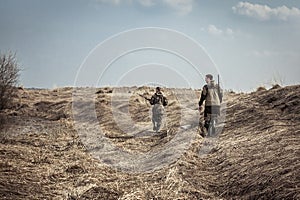 Hunting scene with men hunters with shotguns exploring rural area during hunting season