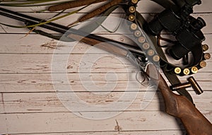 Hunting weapon, bandoleer with cartridges, binoculars on a light wooden background.