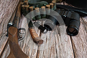 Hunting weapons, bandolier with cartridges, binoculars and a knife on a wooden background.