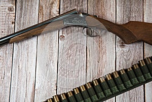 Hunting weapons and bandolier with cartridges on a light wooden background.