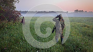 Huntsman and hunter look through binoculars through the fog at wild ungulates