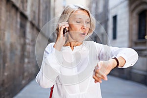 Hurrying woman looks at her watch and talking on the phone