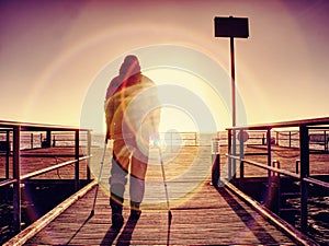 Hurt man with hooded jacket and forearm crutches standing on sea bridge