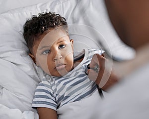 It hurts. Shot of an adorable little boy lying in bed and feeling sick while a paediatrician uses a stethoscope.