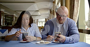 Husband bald and glasses and dark-haired middle-aged wife, sitting in a cafe, eat, communicate. They have on the table