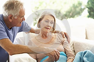 Husband Comforting Senior Woman Feeling Unwell Resting Under Blanket