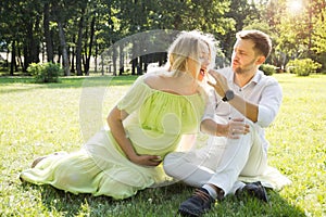 A husband is feeding candy to his pregnant wife on a picnic in the park