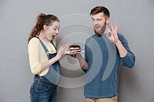 Husband giving plate with chocolae cake to his pregnant wife