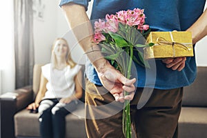 Husband hiding romantic surprise present and flowers behind back to beloved wife