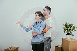 Husband is hugging wife. She is pointing her hands at the copy space for text or product.