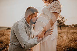husband hugs pregnant wife hold hands on big round tummy kissing belly.