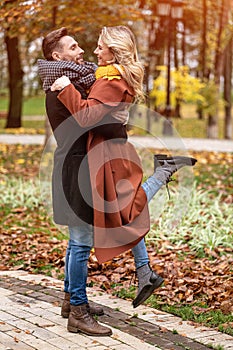 Husband lifting a wife hugged laughing in the autumn park with a cute hug. Outdoor shot of a young couple in love having