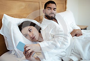 Husband Looking At Cheating Wife Texting On Smartphone In Bedroom