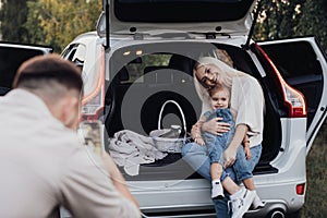 Husband Photographing His Wife and Toddler Daughter That Sitting Inside Opened Trunk of a SUV Car, Family on Road Trip