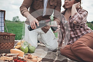 Husband pouring red wine into glass for wife during picnic