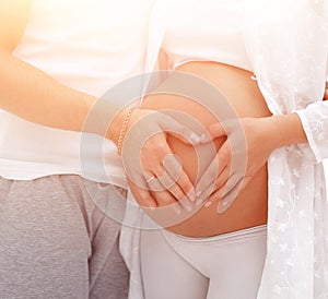 Husband and pregnant wife with folded hands in the shape of a heart on his tummy