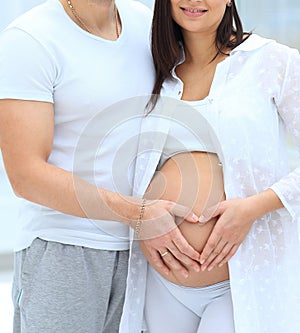 Husband and pregnant wife with folded hands in the shape of a heart on his tummy