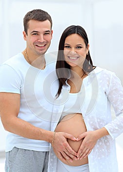 Husband and pregnant wife with folded hands in the shape of a heart on his tummy