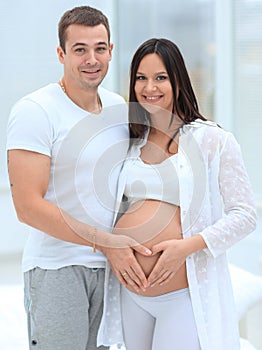 Husband and pregnant wife with folded hands in the shape of a heart on his tummy