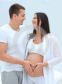 Husband and pregnant wife with folded hands in the shape of a heart on his tummy