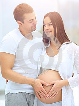 Husband and pregnant wife with folded hands in the shape of a heart on his tummy