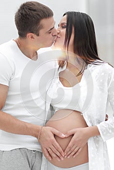 Husband and pregnant wife with folded hands in the shape of a heart on his tummy