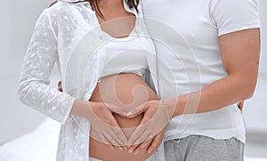 Husband and pregnant wife with folded hands in the shape of a heart on his tummy