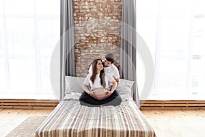 Husband and pregnant wife sitting on a bed