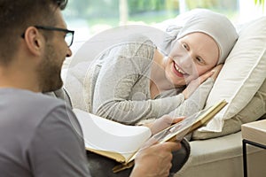 Husband reading a book to a smiling sick woman with headscarf. L