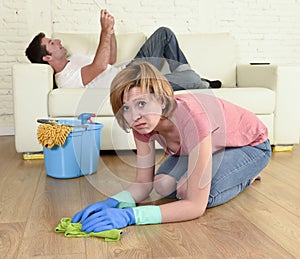 Husband resting on couch while wife cleaning doing housework in chauvinism concept