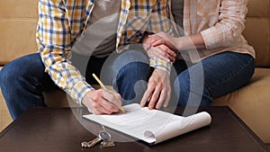 Husband signs apartment purchase contract near wife on sofa