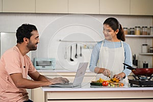 Husband spending time while working on laptop with meal or food preparing wife at kitchen - concept of spending time
